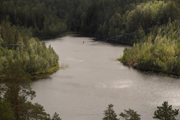 Um homem caminha em um slackline sobre um pitoresco lago na floresta