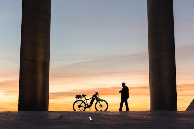 Um homem caminha para sua bicicleta no fundo do pôr do sol