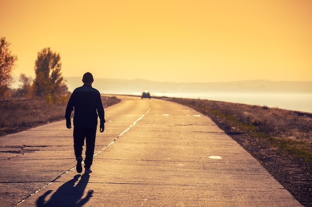Um homem caminha por uma estrada de concreto ao longo do mar em um pôr do sol dourado e olha para a montanha