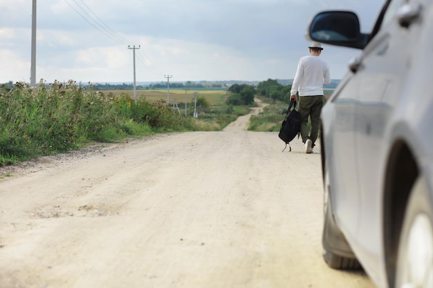 Um homem caminha por uma estrada rural Mochileiro pelo país Um homem para um carro que passa na estrada