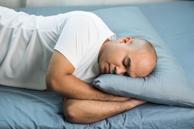 Um homem careca asiático com cerca de 30 anos em uma camiseta branca está dormindo