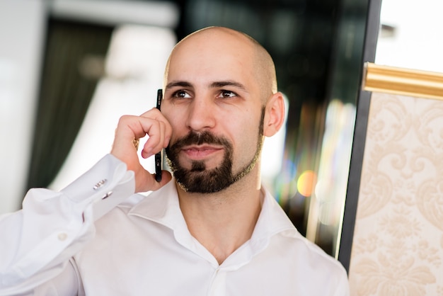 Um homem careca brutal falando ao telefone.