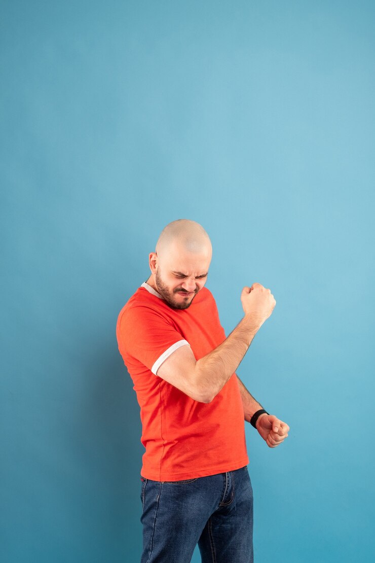 Foto um homem careca de meia-idade com uma barba em uma camiseta vermelha sobre um fundo azul fica com os braços estendidos e se alegra com a vitória. isolado.