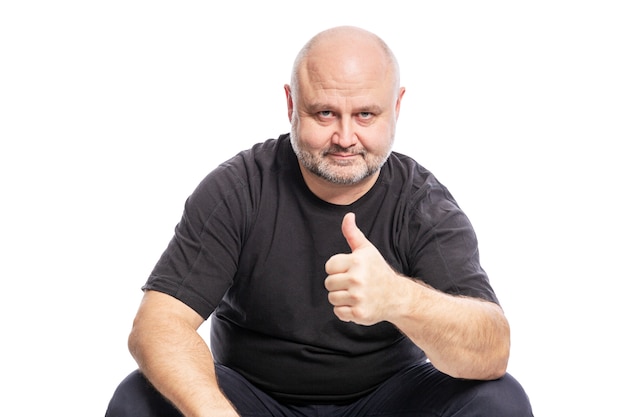 Um homem careca de meia-idade, sorridente, de camiseta preta, está sentado com o polegar para cima. Isolado sobre o branco