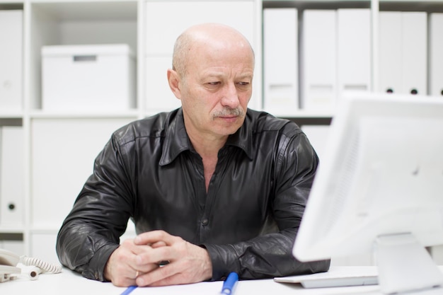 Um homem careca idoso no computador Pensionista no local de trabalho