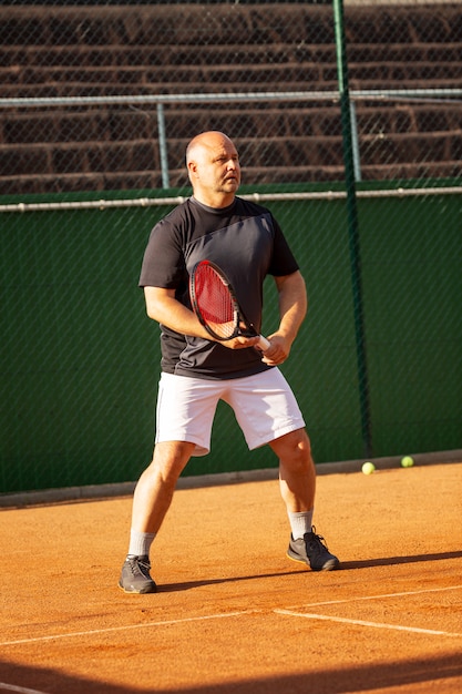 Um homem careca joga tênis na quadra em um dia ensolarado. Saúde e atividade. Vertical.
