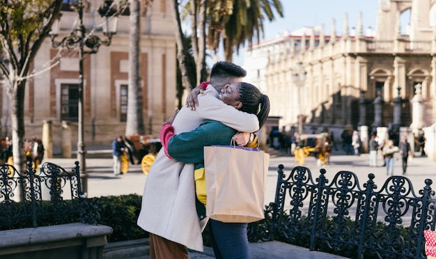 Um homem caucasiano e uma mulher africana se abraçando enquanto seguram sacolas com presentes ao ar livre