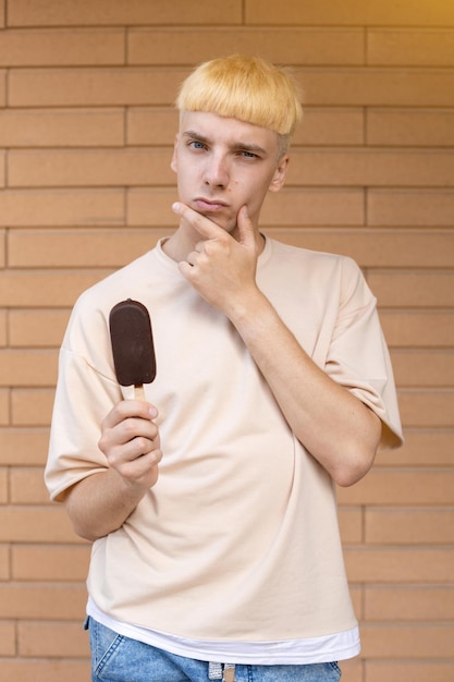 Um homem caucasiano pensativo vestido com uma camiseta bege e segurando um sorvete de chocolate no palito