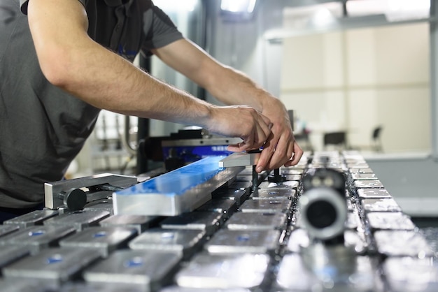 um homem coloca uma peça de alumínio em uma máquina cnc e prepara uma máquina de processamento.