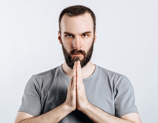 Um homem com as palmas das mãos cruzadas. O cara lê uma oração com as palmas das mãos cruzadas na frente dele. Retrato de jovem bonito n fundo branco com espaço para simulação de publicidade