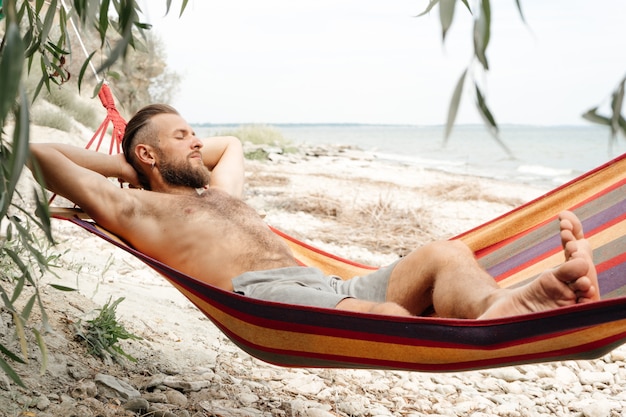 Foto um homem com barba à beira-mar em uma rede está descansando