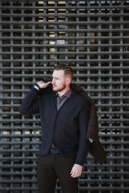 Um homem com barba de terno e suéter azul posa para anunciar roupas masculinas no inverno. Anuncie roupas masculinas