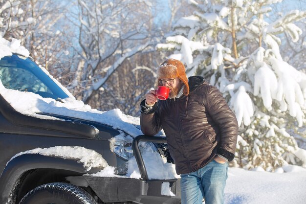 um homem com barba e bigode, usando um chapéu de pele e jaqueta em um dia ensolarado em uma floresta de inverno