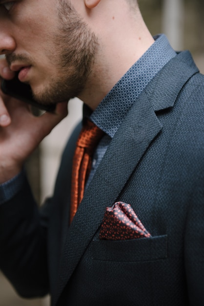 Um homem com barba e óculos escuros em um terno cinza posa na rua para anunciar roupas masculinas.