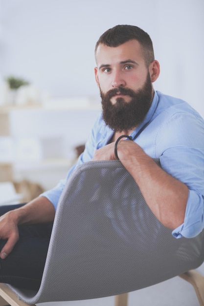 Um homem com barba está sentado em uma cadeira.