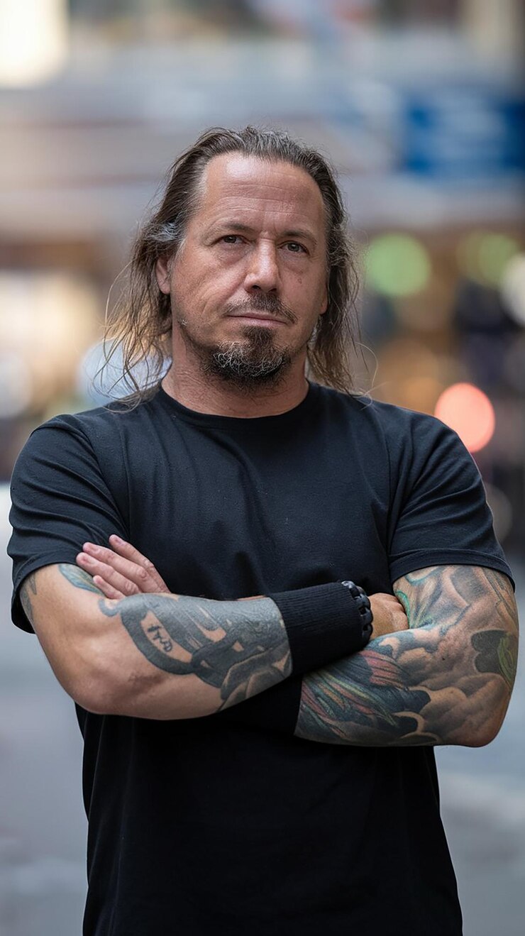 Foto um homem com cabelo longo e uma tatuagem no braço.
