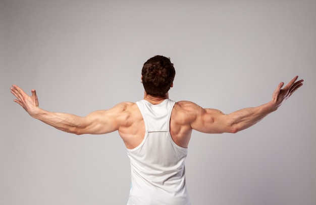 Foto um homem com corpo musculoso abre os braços para o lado e olha para cima