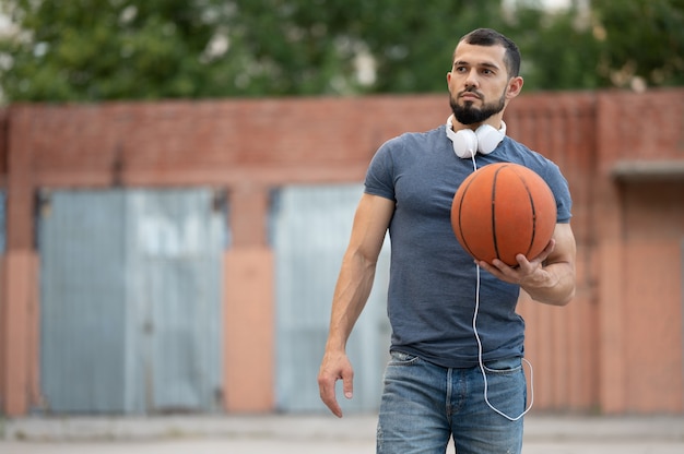 Foto um homem com fones de ouvido está na rua com uma bola de basquete nas mãos