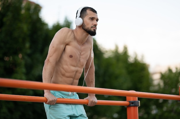 Foto um homem com fones de ouvido fazendo push ups nos bares na rua durante o dia