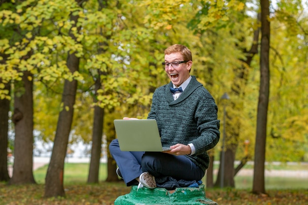 Um homem com lap top em um pedestal que finge ser uma estátua no parque outono. Obter ideia