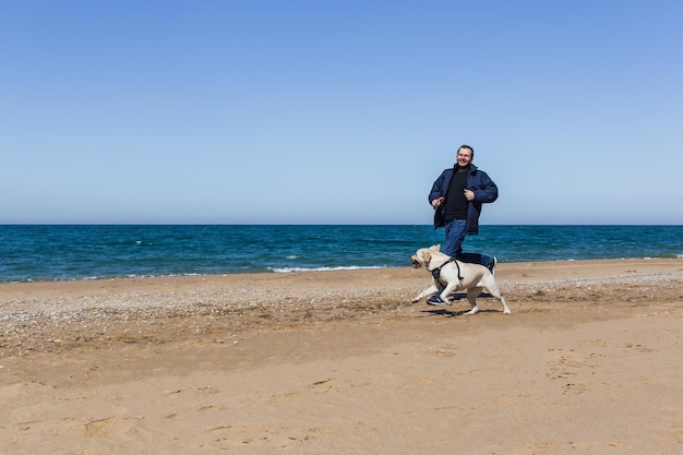 Um homem com roupas de inverno corre ao longo de uma praia com um cachorro em munição