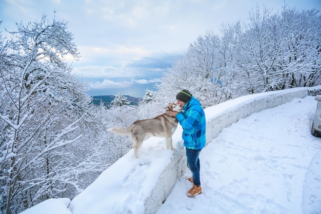 Um homem com roupas quentes está parado com um cachorro ao longo de uma estrada na montanha nevada