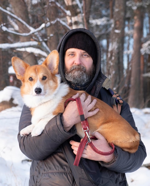 Um homem com seu cachorro Red Welsh Corgi Pembroke no fundo de uma floresta no inverno