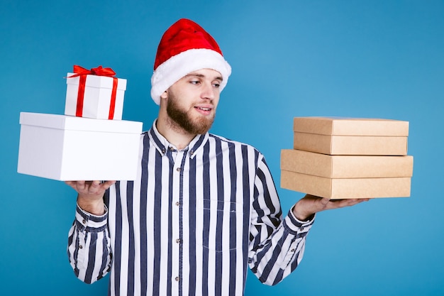 Um homem com um chapéu de Natal segurando caixas de presente em um fundo azul