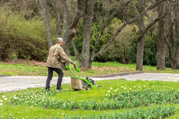 Um homem com um cortador de grama corta a grama no parque