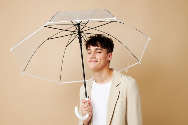 Um homem com um guarda-chuva aberto em uma proteção de jaqueta do fundo bege da chuva