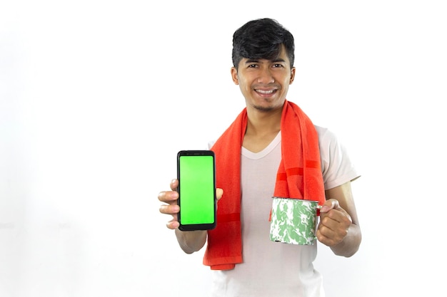 Um homem com um lenço no pescoço segura um telefone e uma caneca com tela verde.