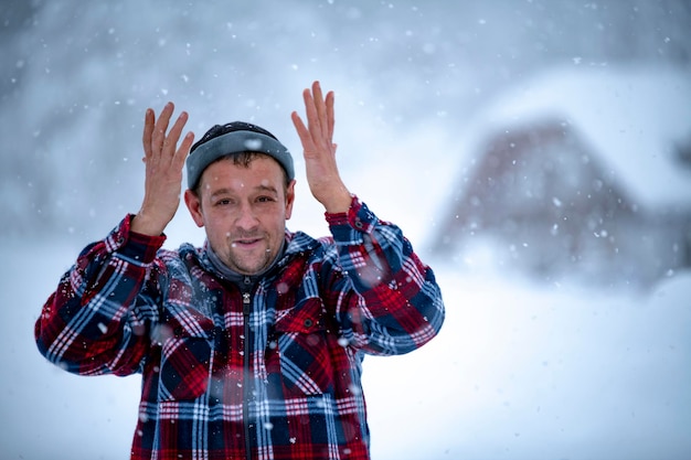 Um homem com um paletó xadrez vermelho está segurando uma xícara de chá nas mãos durante uma nevasca, tendo como pano de fundo lindos montes de neve e uma floresta