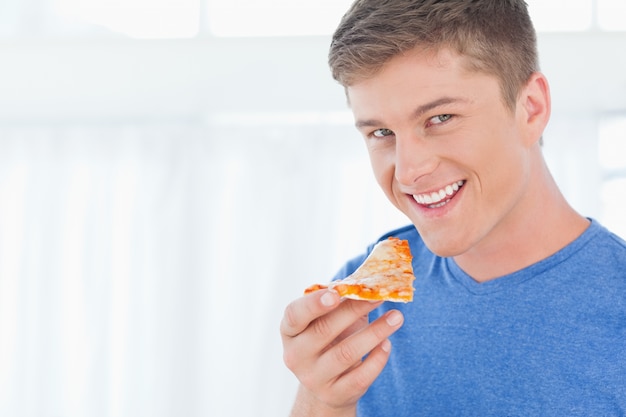 Um homem com um pedaço de pizza enquanto olha para a câmera