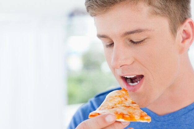 Um homem com um pedaço de pizza perto da boca