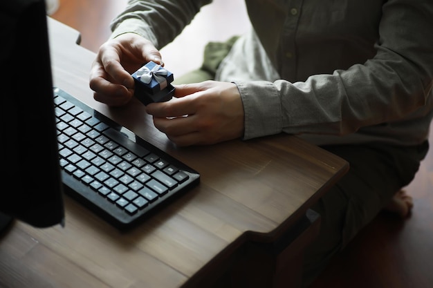 Um homem com um presente na mão senta-se em frente à tela do monitor Encomende um presente para casa e escritório