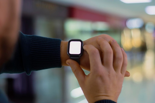 Um homem com um smartwatch e uma maquete de tela branca na mão Um homem usa um rastreador de fitness no fundo de um shopping