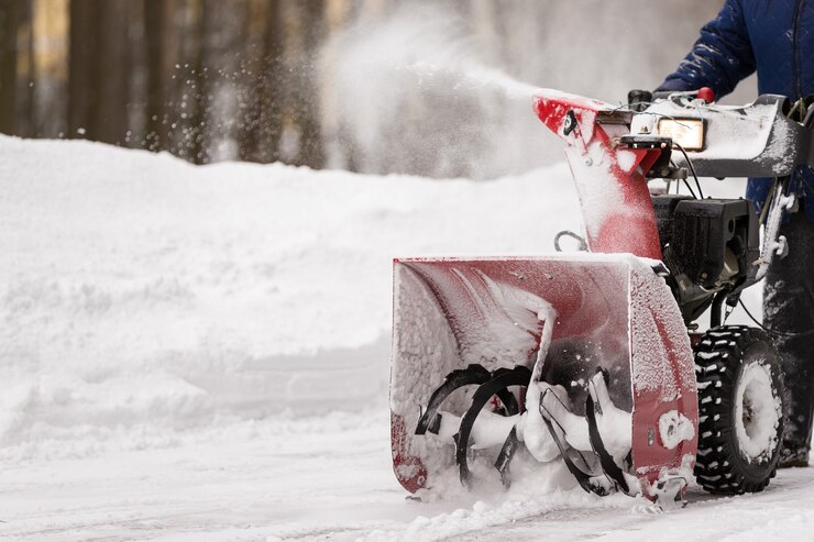 Um homem com um soprador de neve coberto de neve vermelha limpa a área da neve