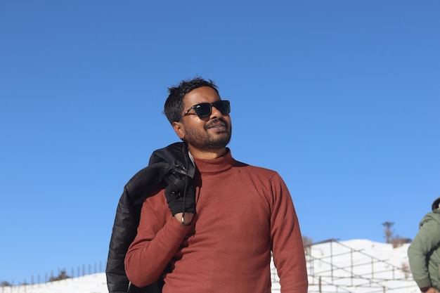 Foto um homem com um suéter vermelho e óculos de sol fica na frente de um céu azul claro.