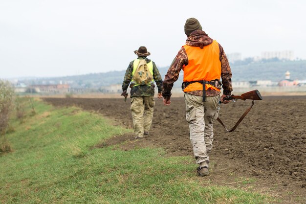 Um homem com uma arma nas mãos e um colete laranja em uma caça ao faisão em uma área arborizada em tempo nublado Caçadores com cães em busca de caça