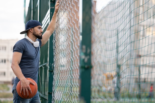 Um homem com uma bola de basquete olha por trás de uma cerca na rua durante o dia