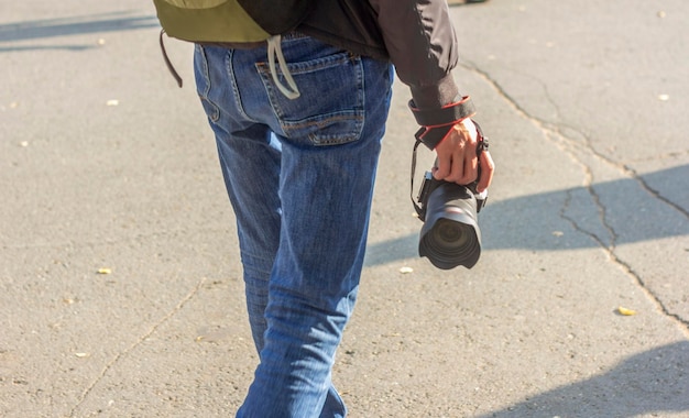 Um homem com uma câmera na mão e uma mochila nos ombros caminha no parque em um dia ensolarado