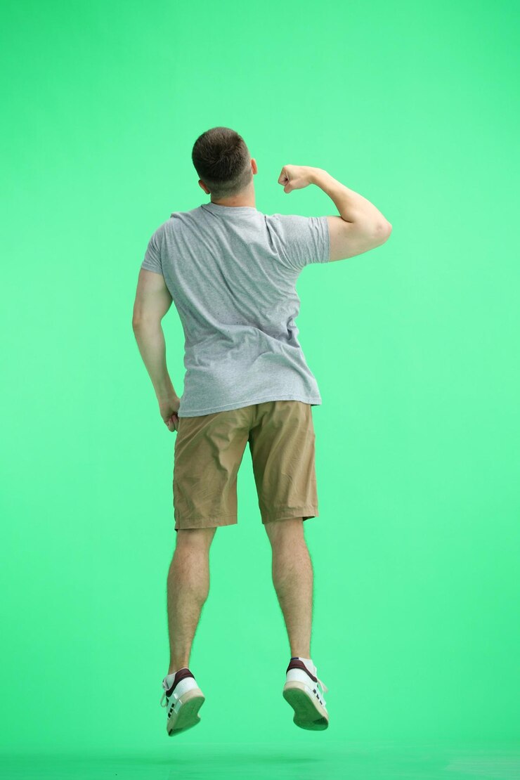 Foto um homem com uma camiseta cinzenta em um fundo verde salta em comprimento