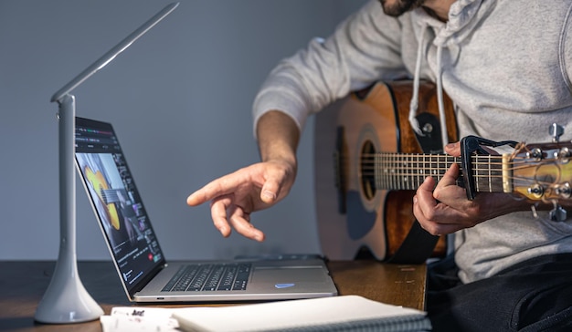 Um homem com uma guitarra na frente de um laptop, tarde da noite, aprende a tocar