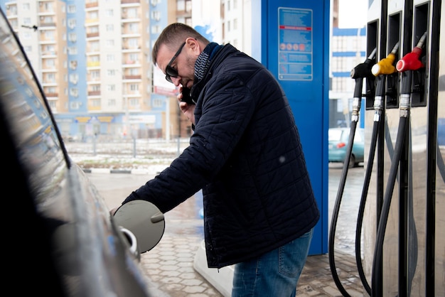 Um homem com uma jaqueta azul e óculos escuros em um posto de gasolina Ele enche o carro Gasolina Lifestile