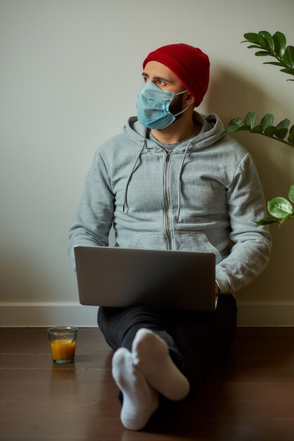 Um homem com uma máscara facial trabalhando em seu laptop