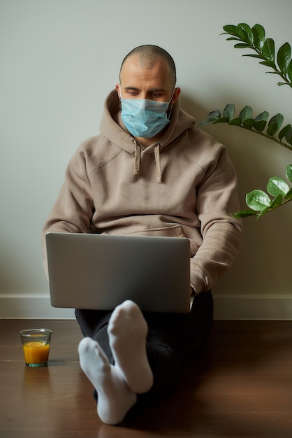 Um homem com uma máscara facial trabalhando em seu laptop