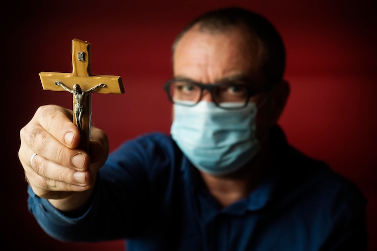 Foto um homem com uma máscara médica descartável com uma cruz católica na mão