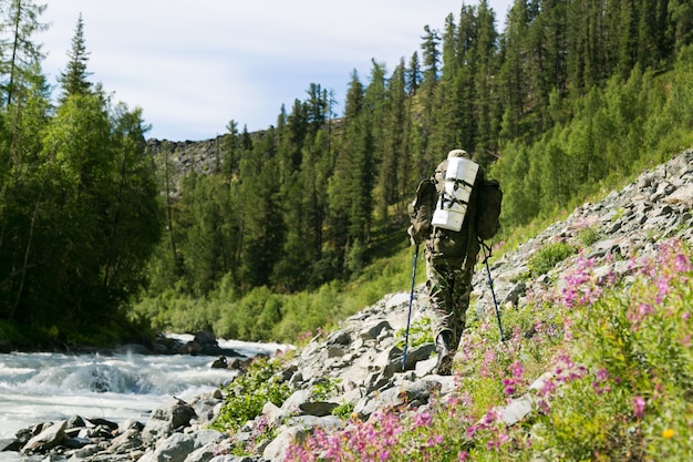 Um homem com uma mochila caminha ao longo de um rio de montanha.