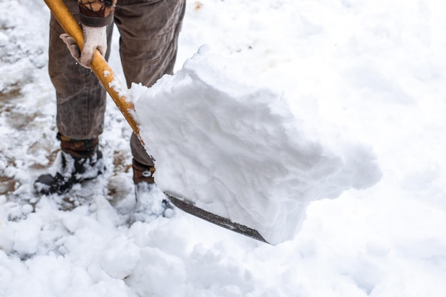 Um homem com uma pá está limpando a neve na rua no quintal de uma casa a neve cai em um dia de inverno mau tempo e precipitação