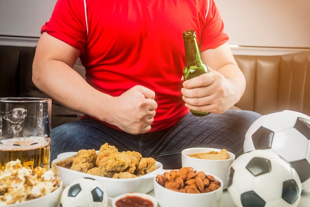 Um homem come lanches e bebe cerveja em casa